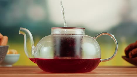 pouring hot water into a glass teapot to brew herbal tea
