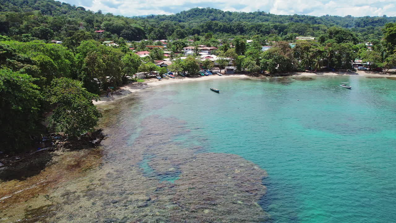 An epic aerial revealing a lush, scenic beach with boats in the turquoise clear water in Puerto Viejo, a popular tourism destination on the Caribbean coast of Costa Rica.