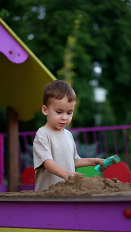 dark-haired baby boy plays with sand outdoors. kid moves the sand with a shovel. vertical video.