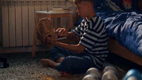 boy repairing baseball glove in his bedroom