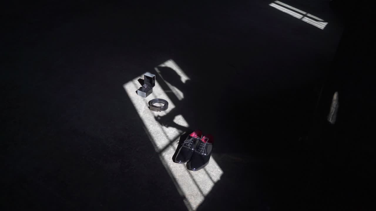 disparo creativo en cámara lenta de la sombra de un novio que se arroja en estos accesorios mientras se está vistiendo