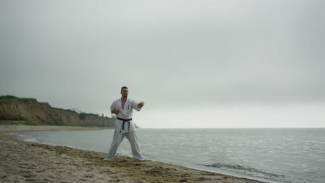 Luchador-De-Judo-Haciendo-Ejercicio-En-La-Playa-De-Arena.-Hombre-Entrenando-Técnica-De-Combate.