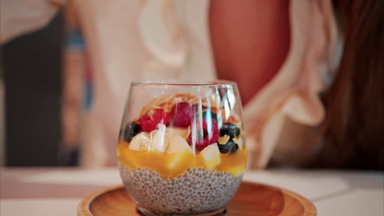 Close up of a woman eating chia pudding with fruit at a cafe