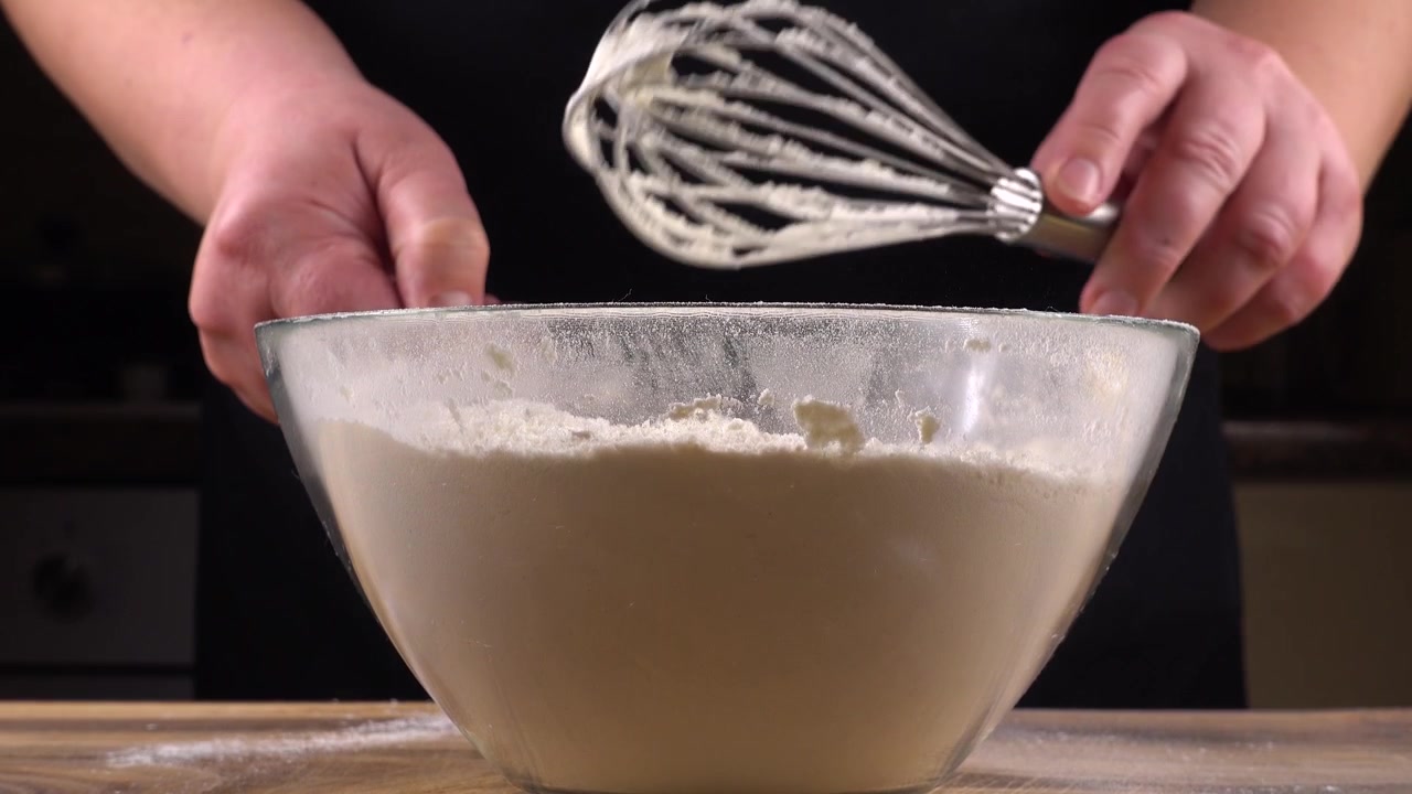 Stirring the flour mixture with a whisk in a glass bowl on the background of the kitchen.