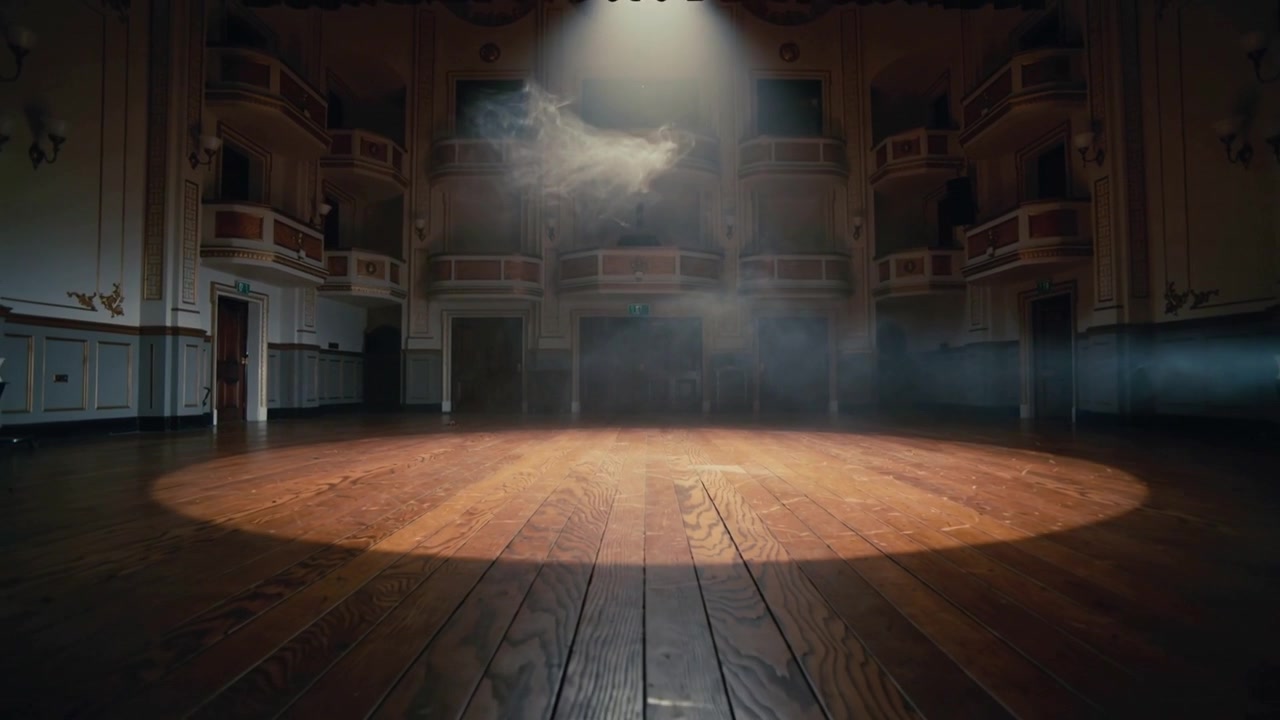 Shining overhead spotlight casting round pool on wooden stage at theater, preparing show with haze