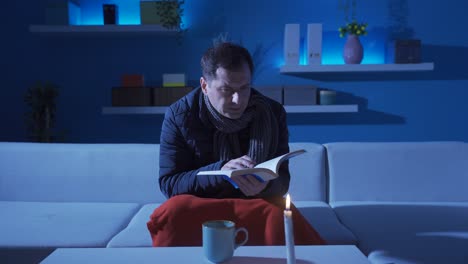 hombre leyendo un libro a la luz de las velas en la oscuridad.