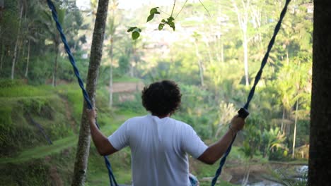 Slow-Motion-shot-of-a-male-Caucasian-Tourist-Swinging-on-a-swing-over-the-rice-paddies-at-the-Tegallalang-Rice-Terraces-in-Bali,-Indonesia