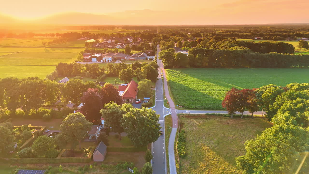 Rural sunset with road view. Sun sets over a picturesque countryside, illuminating fields and homes along a winding road