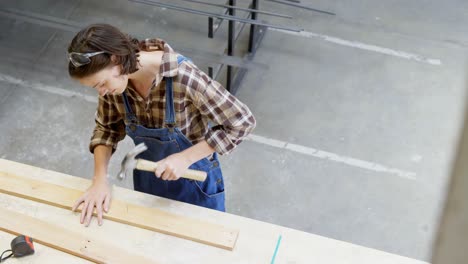 female welder hammering nail on a wooden plank 4k