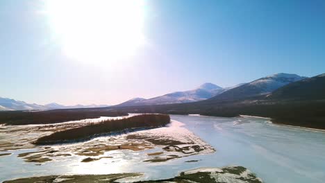 Flug-über-Einen-Gefrorenen-Fluss-Und-Einen-Grauen-Wald-Im-Sonnigen-Jakutien-Aus-Der-Vogelperspektive-4k