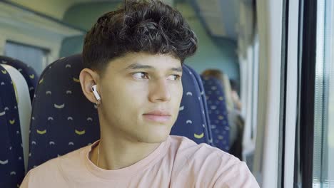 young man traveling with the train and listening to music while looking outside