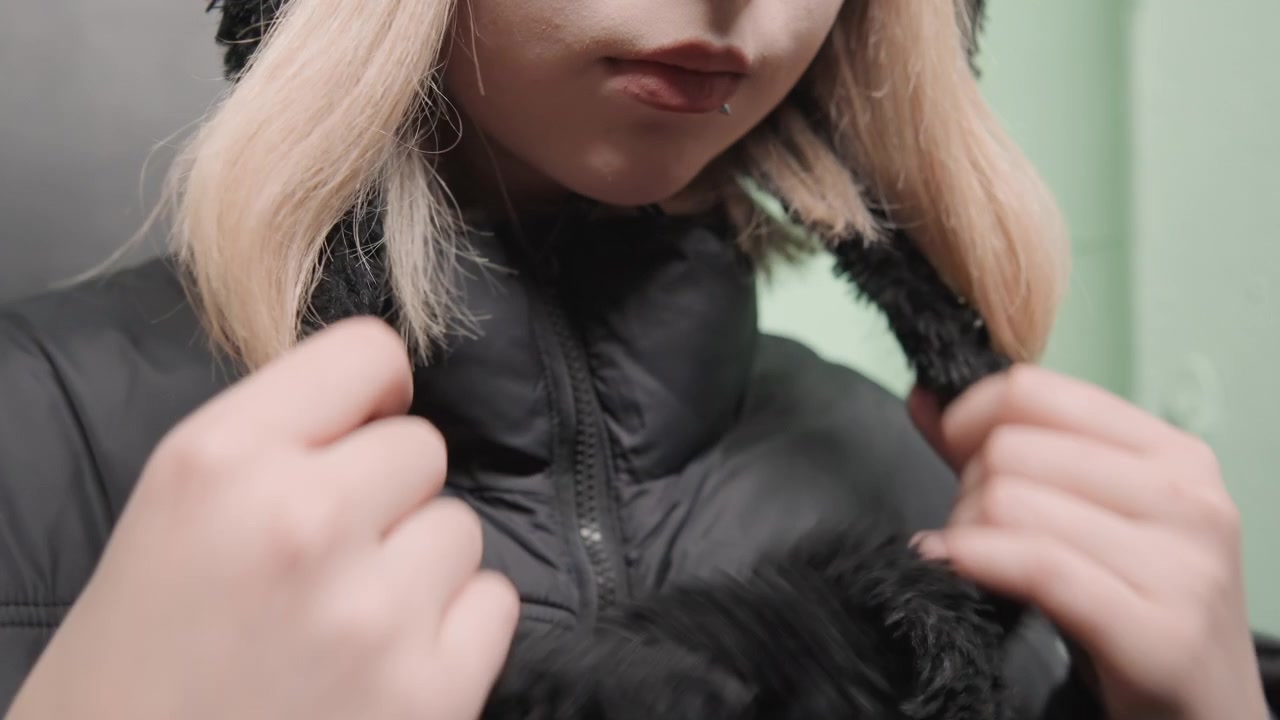 Donna bianca che annoda la sciarpa con cura, giacca a piumino e scaldacollo in maglia, dita delicate che avvolgono il tessuto, ingresso interno, sfondo verde tenue, dettaglio ravvicinato della texture, umore introspettivo in cerca di calore.