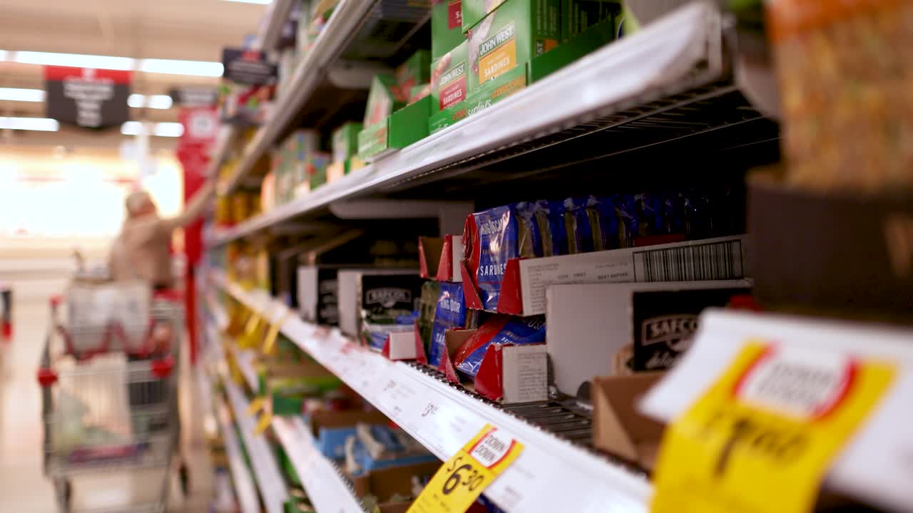 A shopper navigates a snack aisle in a well-lit Gold Coast supermarket, examining products on the shelves