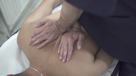 a chiropractor cracks the upper middle back portion of a young adult caucasian male patient as he lies topless face down on a massage table in a physiotherapy clinic, closeup top-down view