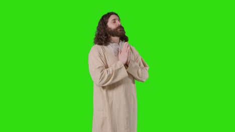 studio shot of man wearing robes with long hair and beard representing figure of jesus christ praying on green screen 1