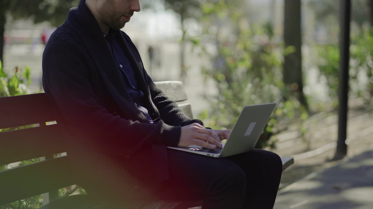 Concentrated man sitting on bench and working with laptop