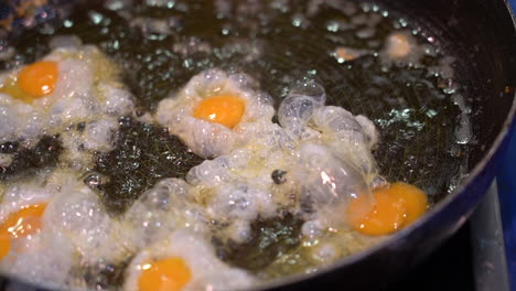 closeup of a man frying small quail eggs in a pan with plenty of oil