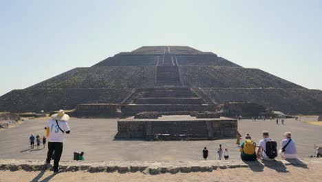 wide, handheld shot of tourists looking at the ancient pyramid of the sun at the archaeological site of teotihuacan in mexico, on a clear, sunny day