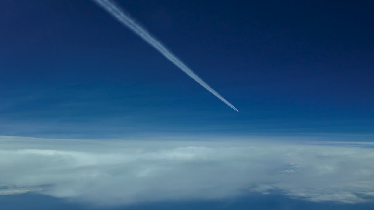POV vliegtuigspoor dat zeer hoog vliegt in een bewolkte lucht met een diepblauwe hemel