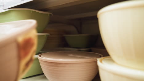 view of a hand taking a bowl from the bowl section in a store. the scene includes various bowls, such as green and brown ones, neatly arranged on shelves