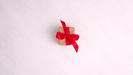 gift box with red ribbon spinning on pink wood background. 360 degree rotation. seamless loop. concept sales, discount price, christmas holidays and shopping