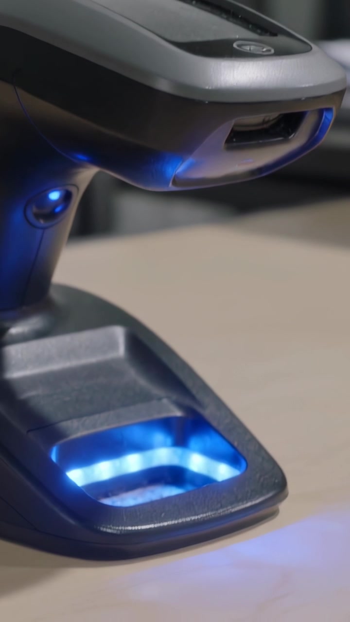 Vertical video: Lowering camera revealing barcode scanner in cradle at desk, showing blue LED well