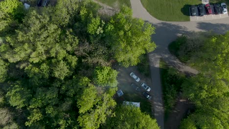 Rising-birds-eye-view-over-campsite-in-the-forest-with-vehicles-parked-next-to-campground-during-a-sunny-and-hot-summer-afternoon