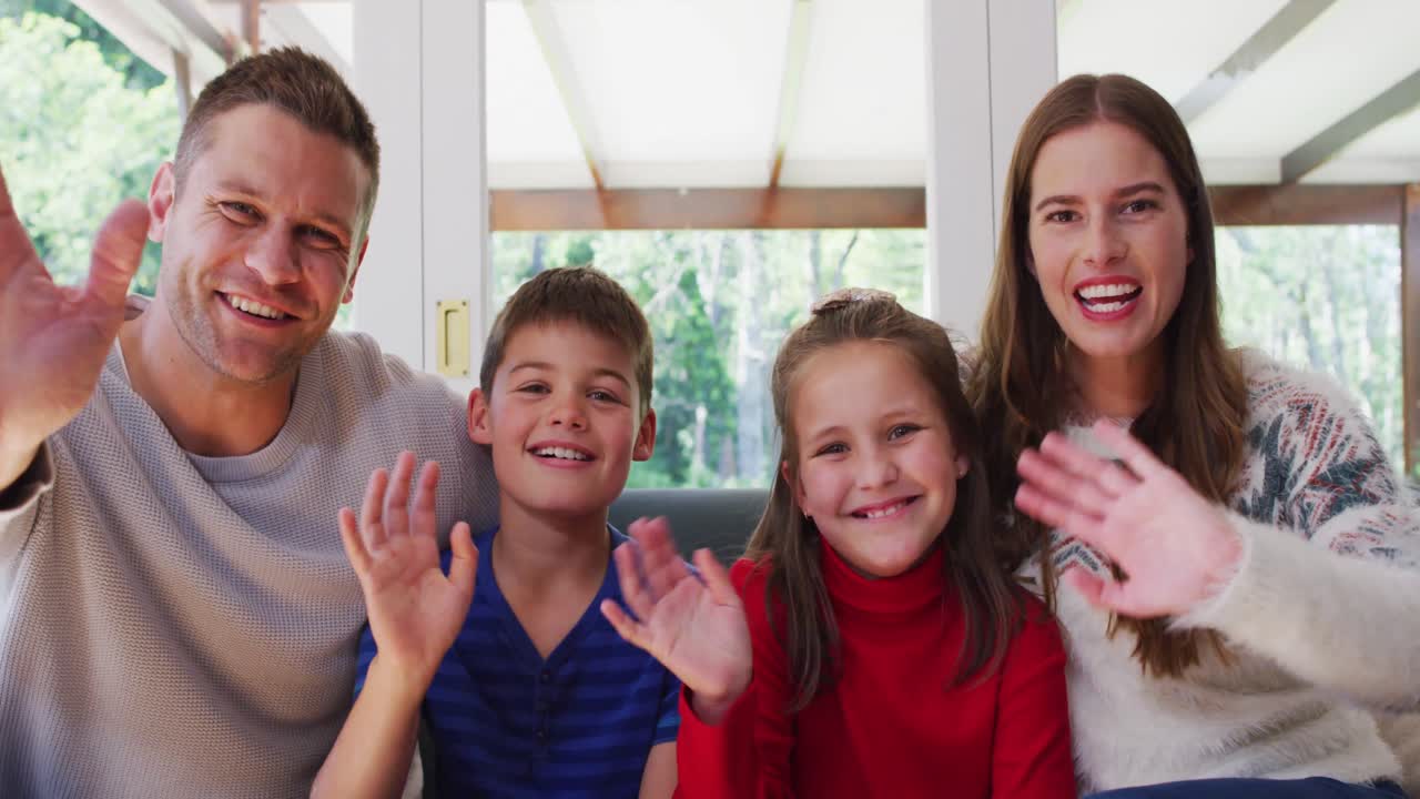 카우카시안 가족의 초상화 웃고 카메라를 흔들며 소파에 앉아 있습니다.