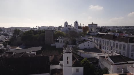 Antena-Orbitando-Sobre-El-Paisaje-Urbano-De-Tavira,-Con-La-Iglesia-De-Santa-María-En-La-Distancia,-Día-Soleado