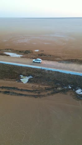 a drone view shows a car driving forward on a straight road in kutch, gujarat, india with endless golden dunes stretching on both sides under a clear sky, capturing a surreal desert journey 4k fpv