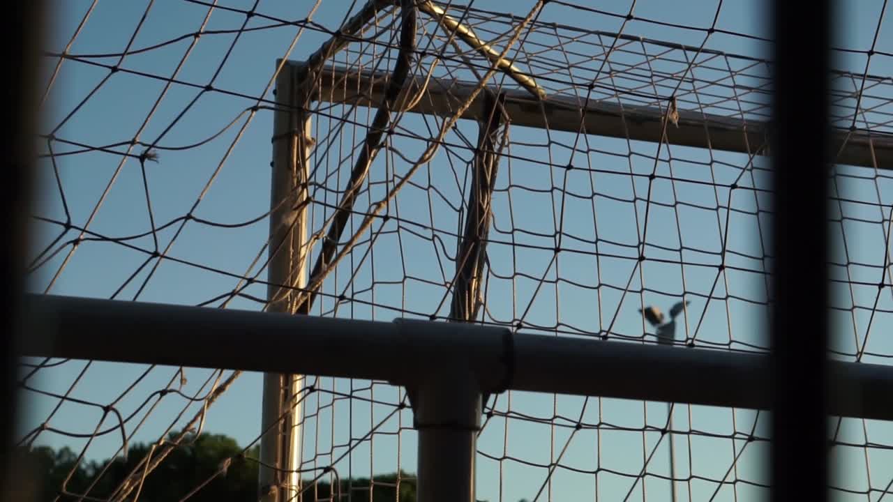 Ripresa dal basso verso l'alto dell'angolo di una porta da calcio attraverso sbarre e reti