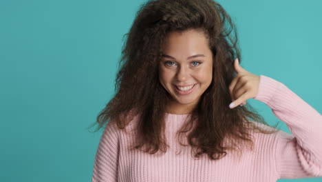 caucasian curly haired woman making call me gesture in front of the camera.