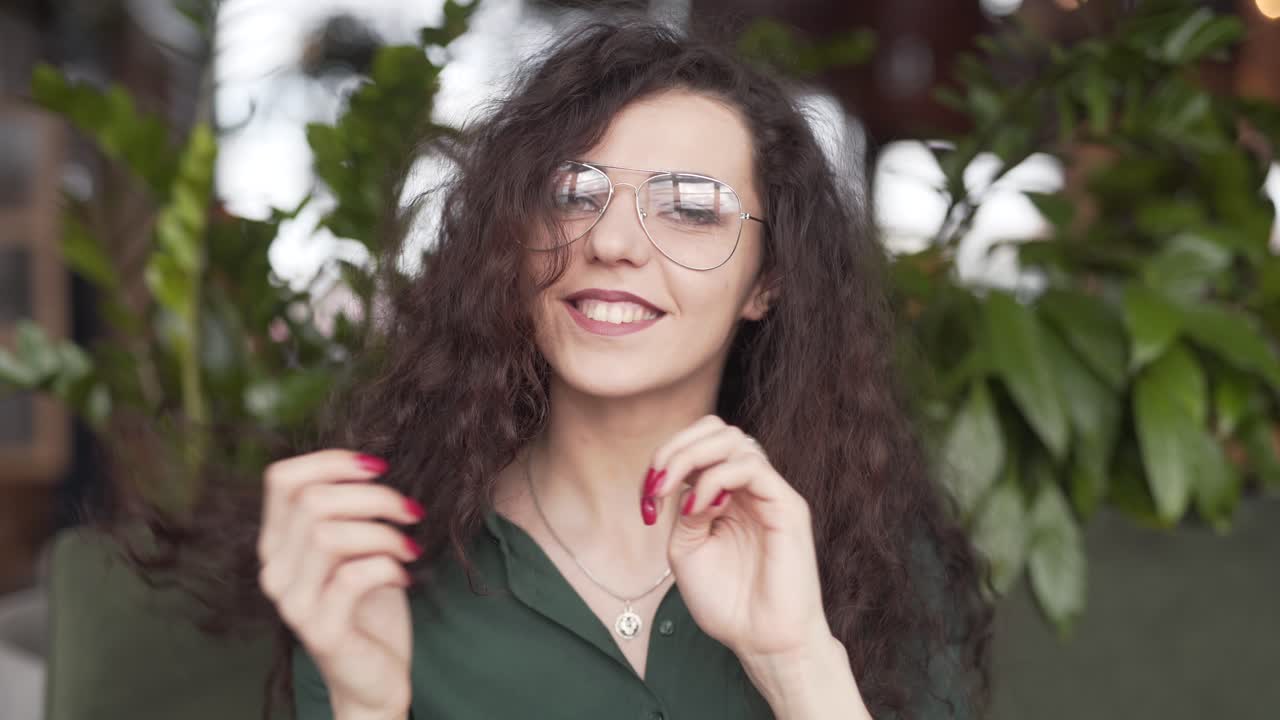 hermosa mujer con gafas juega con su cabello mientras sonríe a la cámara