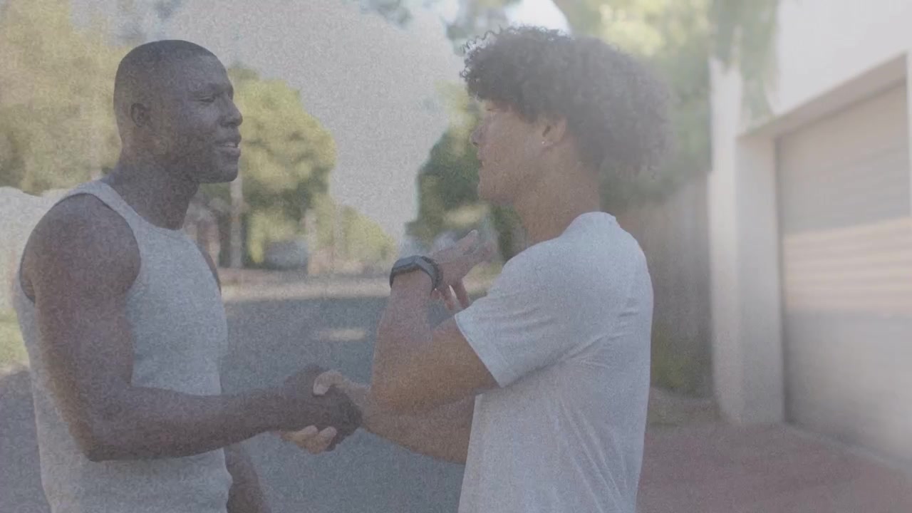 Man wearing smartwatch initiating handshake with other man hugging briefly then talking business