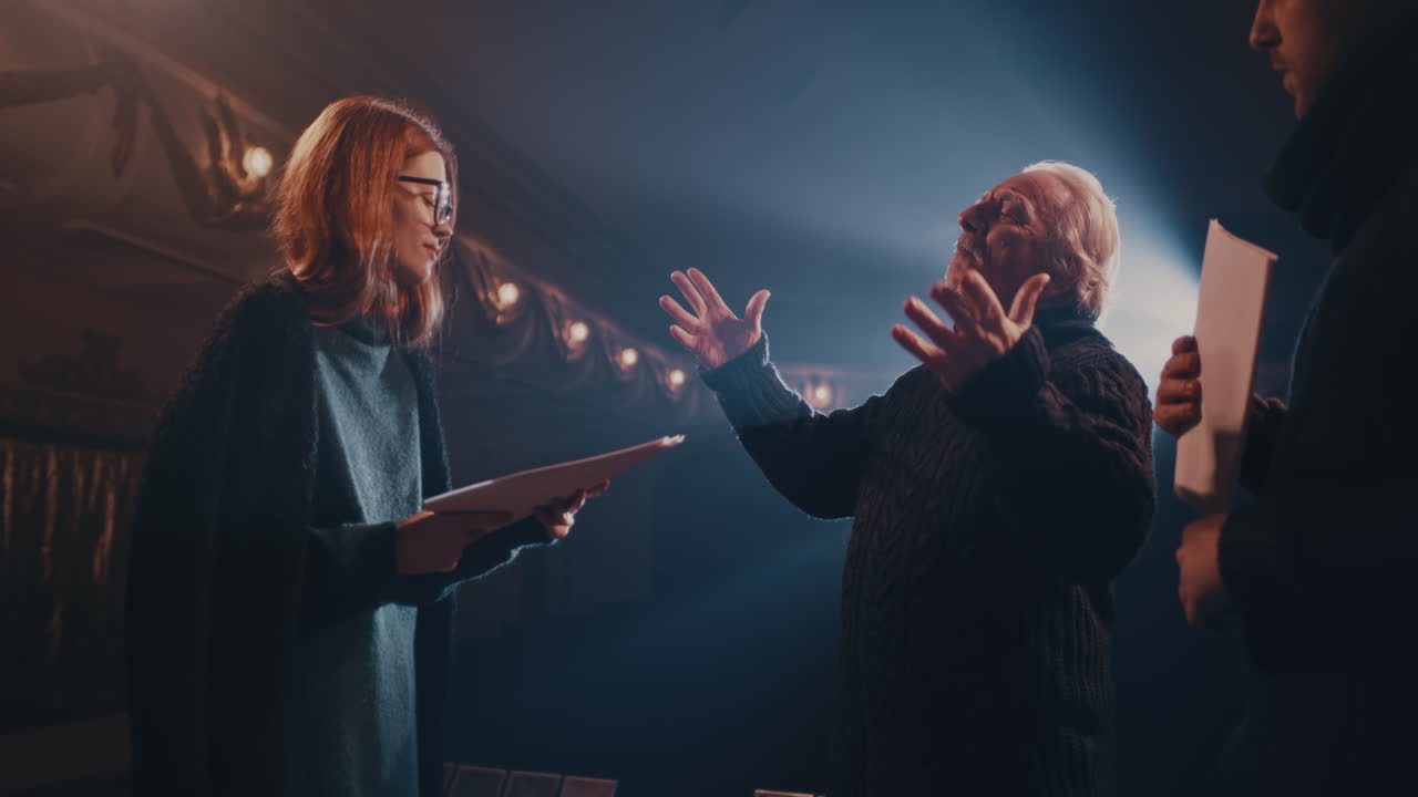 Senior Director Stopping and Talking with Actors during Rehearsal Elderly Stage Director Stopping Man and Woman and Explaining Scene to Actors during Rehearsal in Spotlight in Theater