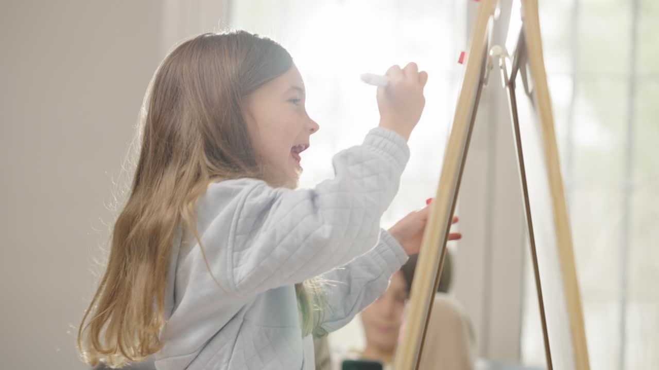 Young girl drawing on an easel with a marker