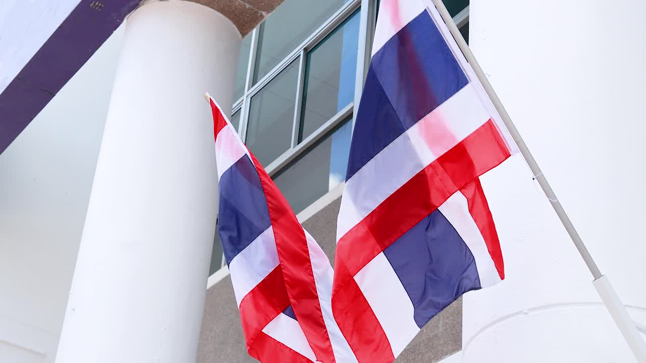 Multiple Thai flags flutter against a building in Phuket, Thailand. Bright daylight highlights the red, white, and blue colors