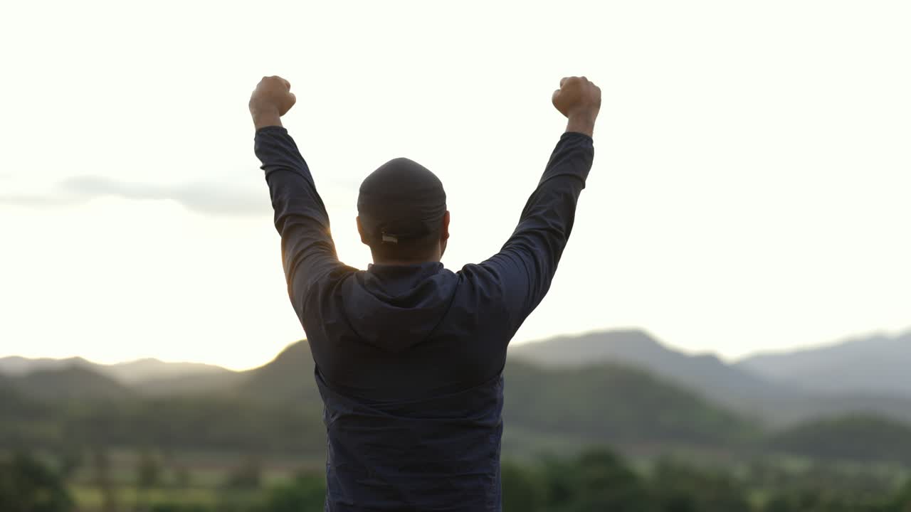 Sportsman standing and raising arms celebrating at the beautiful light. Successful man stand and happily with mountain background at sunset. Success, happy concept