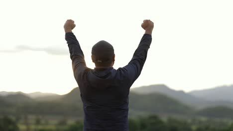 sportsman standing and raising arms celebrating at the beautiful light. successful man stand and happily with mountain background at sunset. success, happy concept