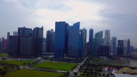 aerial drone shot flying forward towards a line of towering skyscrapers in singapore, showcasing a high-tech, futuristic city vibe