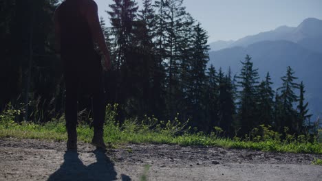 black male traveler walking up to cliff ridge and looking out towards masssive mountain range in switzerland