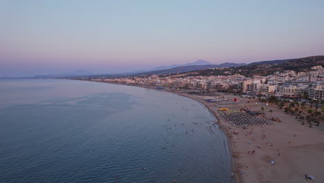 sunset over a tranquil beach town with calm waters and distant mountains