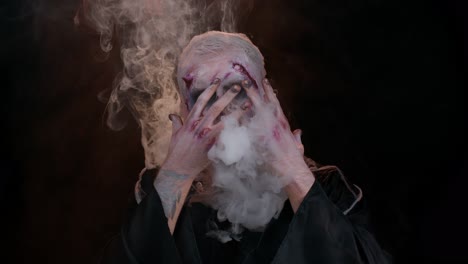 Sinister-man-with-horrible-scary-Halloween-zombie-makeup-in-costume-blows-smoke-from-nose-and-mouth