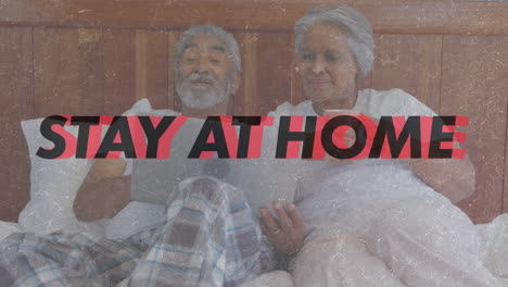 Animation of words Be Safe Stay At Home flashing over senior biracial couple lying in bed