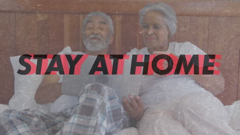 animation of words be safe stay at home flashing over senior biracial couple lying in bed