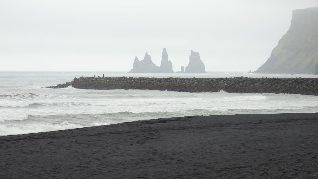 Iceland's black sand beach with rough waves and distant rock formations under a misty overcast sky