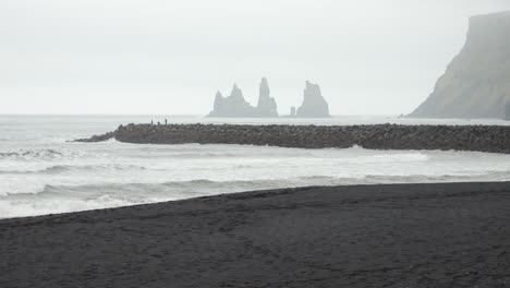 la playa de arena negra de islandia con olas ásperas y formaciones rocosas lejanas bajo un cielo nublado
