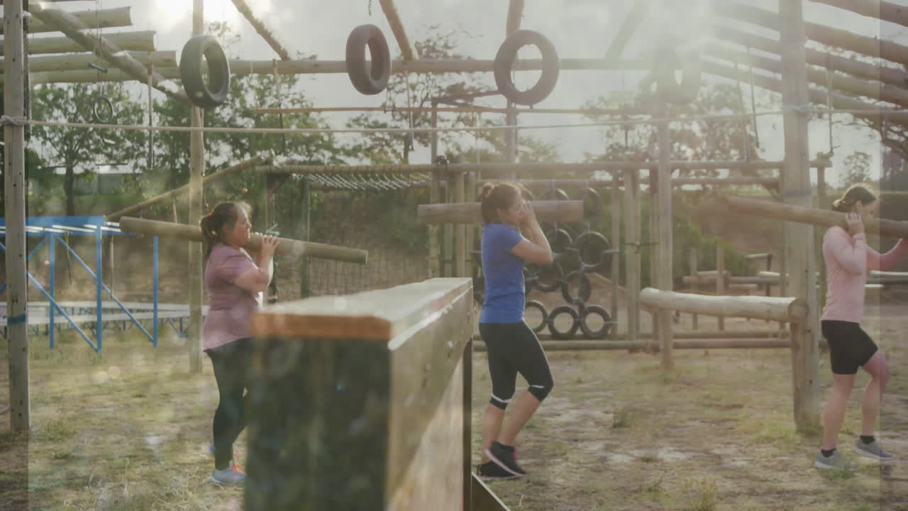 Exercising at outdoor obstacle course, two women navigating wooden and tire structures
