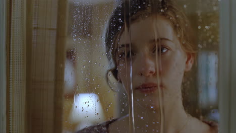 woman looking through a rain-streaked window
