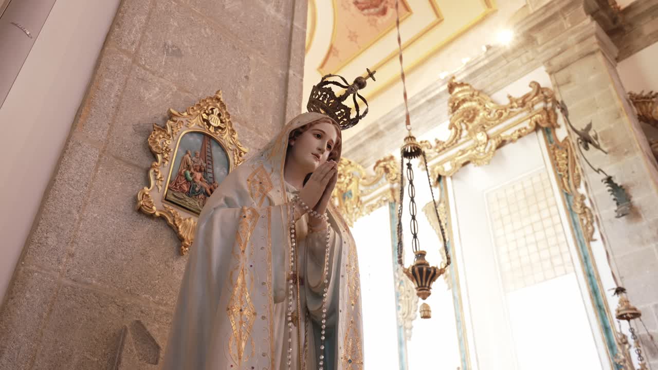 Mid shot of a crowned Virgin Mary statue with praying hands and rosary inside an ornate church